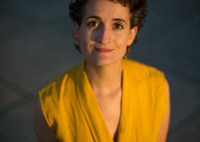 Portrait of Judit Saez in a yellow top, softly lit outdoors