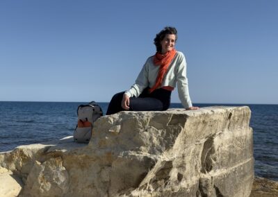 Judit Saez sitting on coastal rocks by the sea, wearing an orange scarf